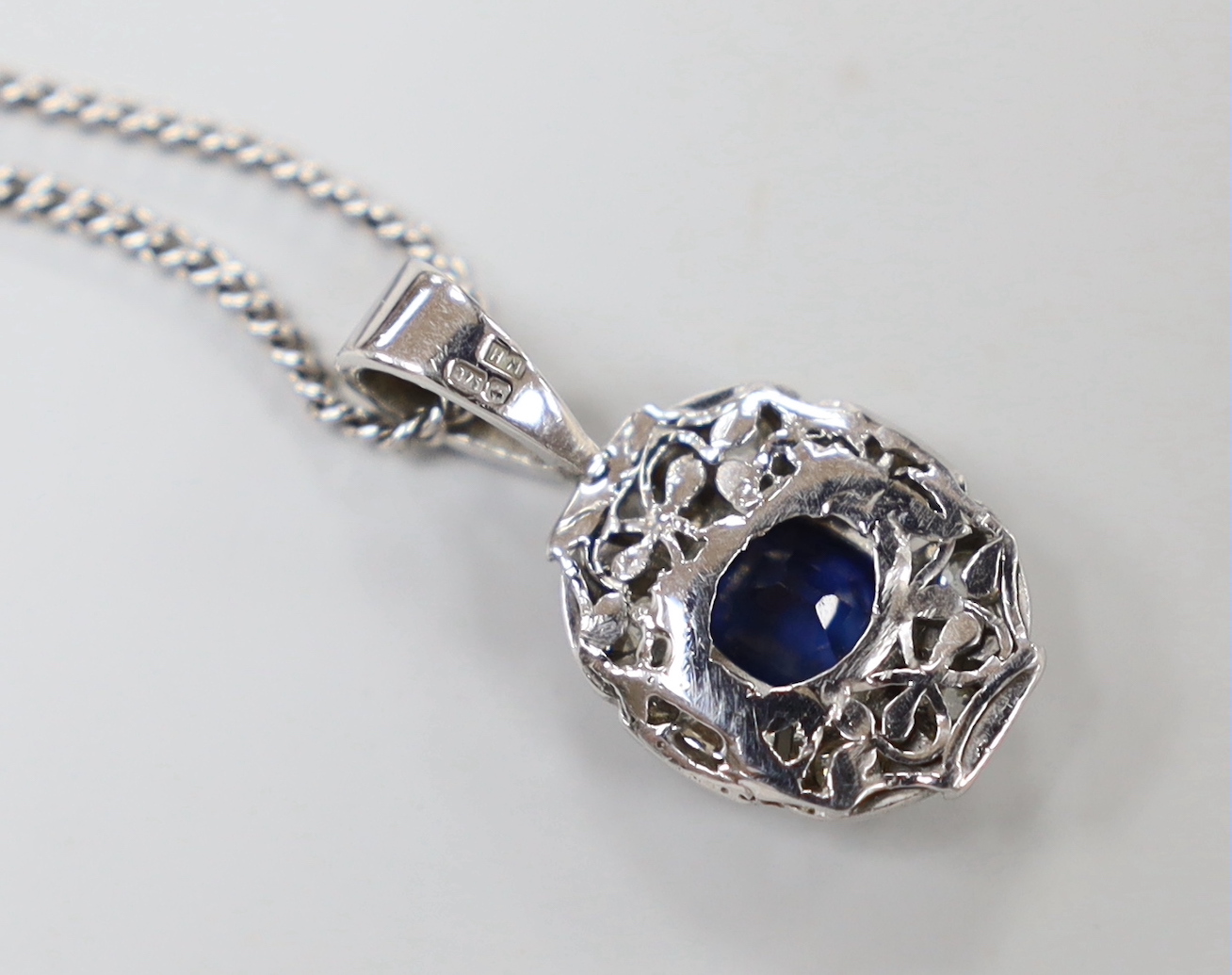 A modern 9ct white gold, sapphire and diamond set oval cluster pendant, 22mm, on a 9ct white gold chain, 60cm, gross weight 8.1 grams.